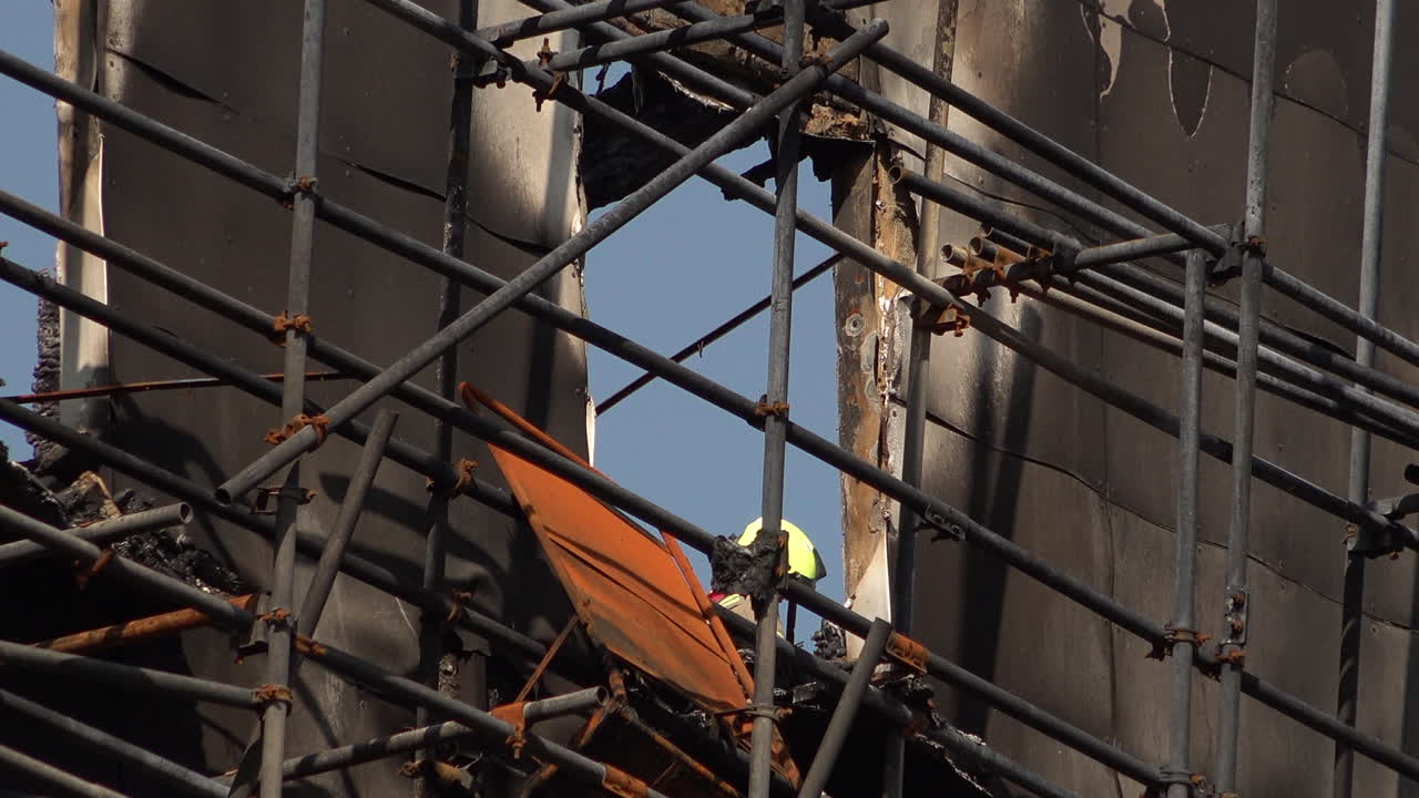 A firefighter appears at a window as they dowse down a tower block covered in flammable cladding that was totally destroyed by a fire.