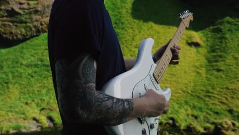 hombre tocando la guitarra frente a una hermosa cascada en islandia