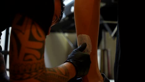 tattoo artist carefully applies a stencil of a dog paw design on the client’s leg to prepare for inking