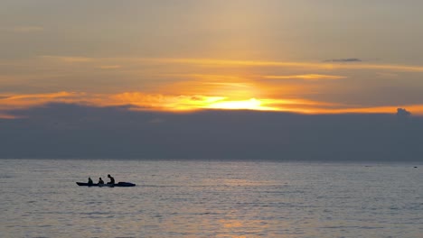 tourists in a rowboat at colorful orange sunset, silhouettes against the setting sun