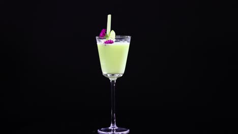 a vibrant green cocktail in a glass with garnish, set against a black background, showcasing elegant presentation