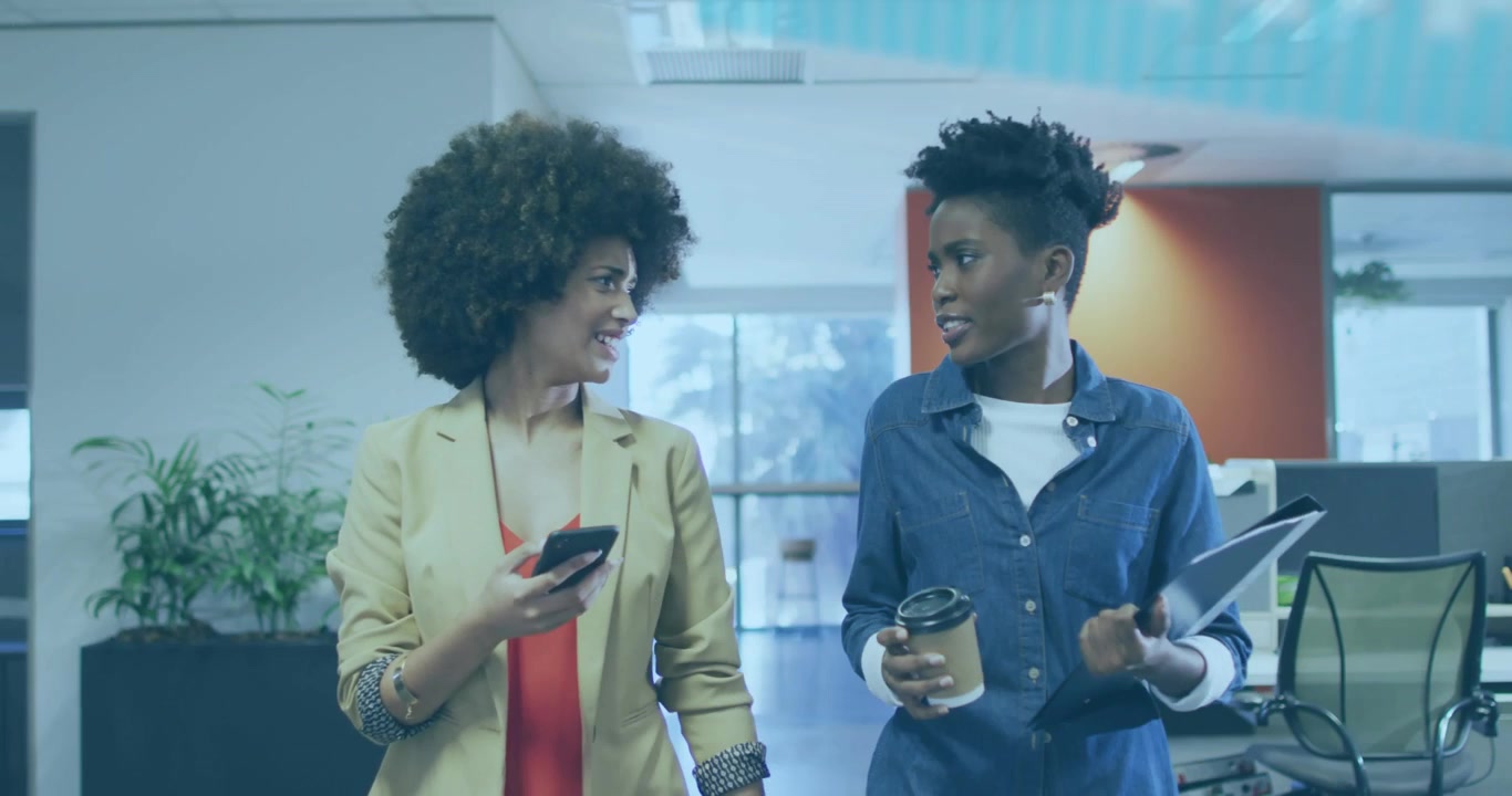 Two coworkers walking office, phone glance initiating business data overlays sliding across frame
