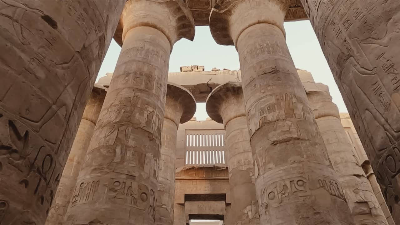 Majestic view of the towering stone columns inside the Karnak Temple complex in Luxor, Egypt. The pillars are adorned with intricate hieroglyphic carvings and symbols from ancient Egyptian history.