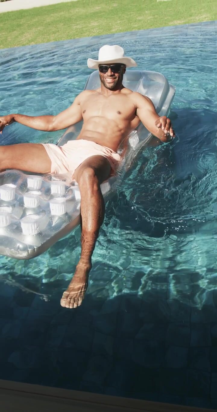 Vertical video: African American man shifting, dipping, paddling, relaxing on clear float at pool
