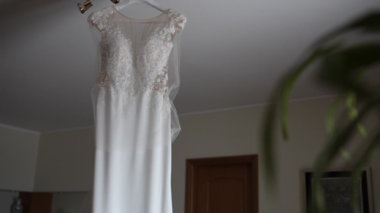 White wedding dress with lace bodice hanging on hanger indoors showing full length garment ready for ceremony
