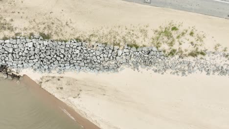 a man walks along the large rocks set against the shoreline