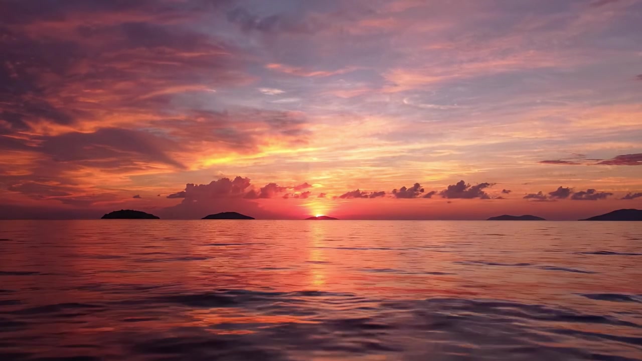 Matahari Terbenam yang Memukau di Atas Perairan Tenang: Tampilan Warna Alam yang Menakjubkan Menerangi Cakrawala dengan Ombak yang Menenangkan dan Pulau-pulau Jauh di Langit Malam