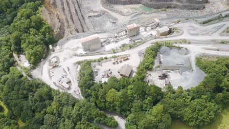 aerial view of a large open-pit quarry with industrial infrastructure and heavy machinery surrounded by green forests.
