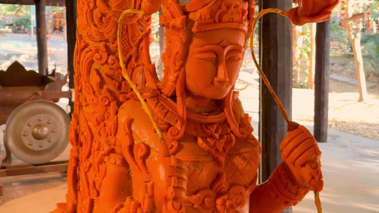 Detailed view of an intricately carved orange candle sculpture with serene facial features and decorative elements.