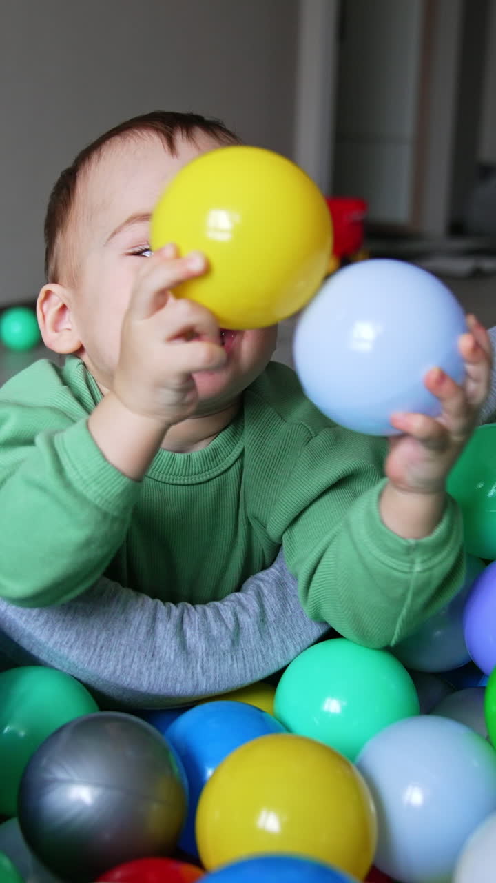 Happy smiling kid leaned on the dry pool and plays with balls. Adorable toddler playing indoors. Vertical video