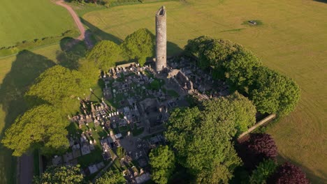 aerial view of ancient ruins, graveyard, and round tower of monasterboice on sunny day in county louth, ireland. pullback shot