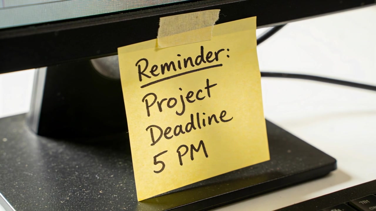 Shifting camera right and down on office desk, revealing sticky note showing project deadline 5PM