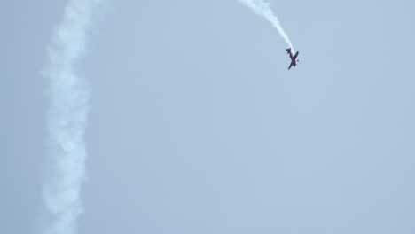 single red aerobatic airplane climbs vertically with smoke trail during an airshow under clear sky