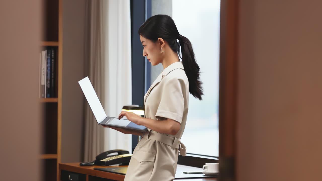集中してオンラインで仕事をするビジネスウーマン。ノートパソコンを使い、日記にメモを取りながら遠くを見つめ、タイピングやメール送信、To-Doリストのチェックを行う。