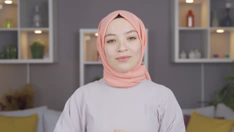 young girl straightens hijab, looking at camera.