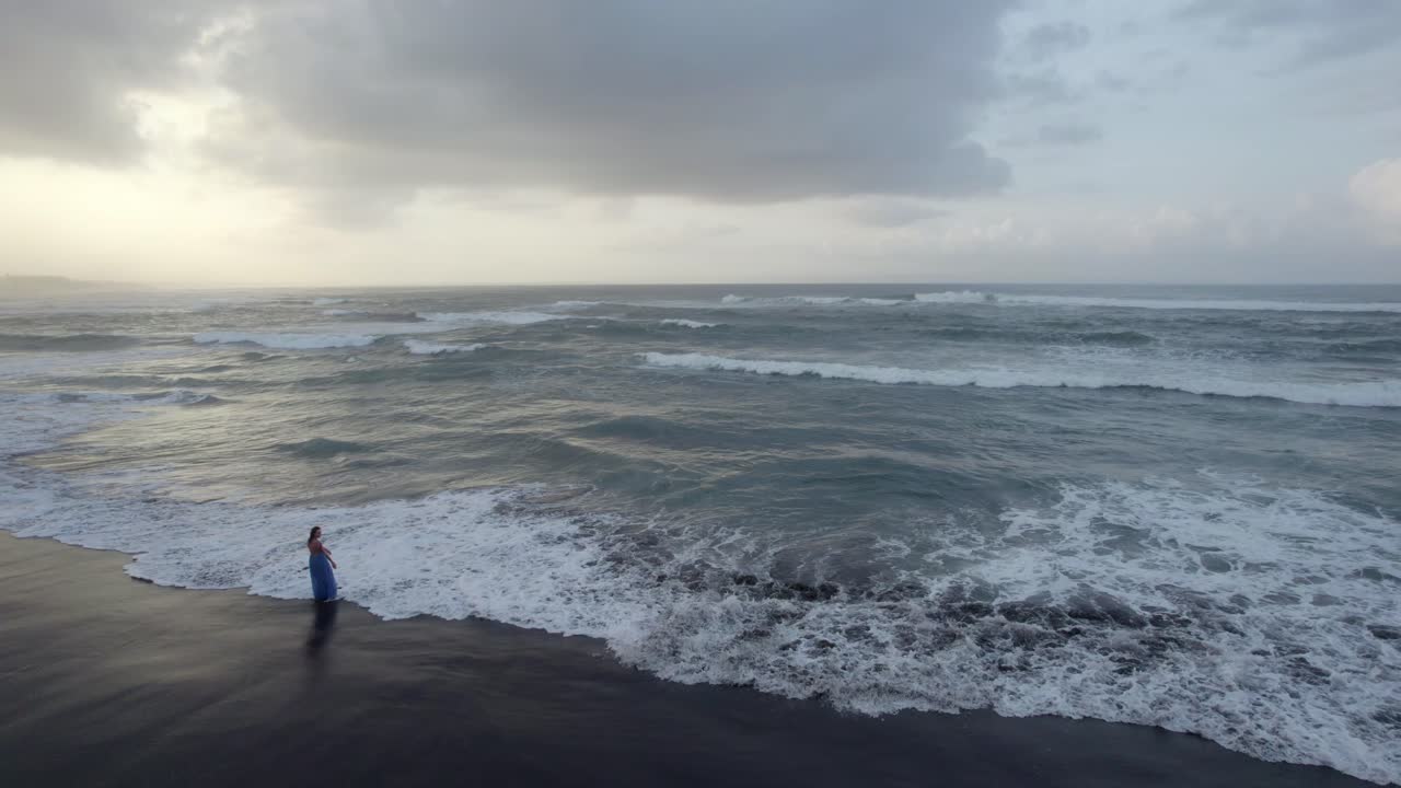 푸른 드레스를 입은 여성의 에어리어가 일몰 때 바다 파도와 함께 열대 낙원 모래 해변에서 삶을 축하합니다.