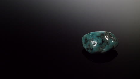 una piedra mineral azul turquesa aislada sobre un fondo negro reflectante