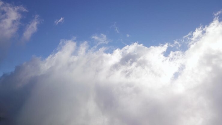 Billowing white clouds grow wispy tendrils reaching up into blue sky