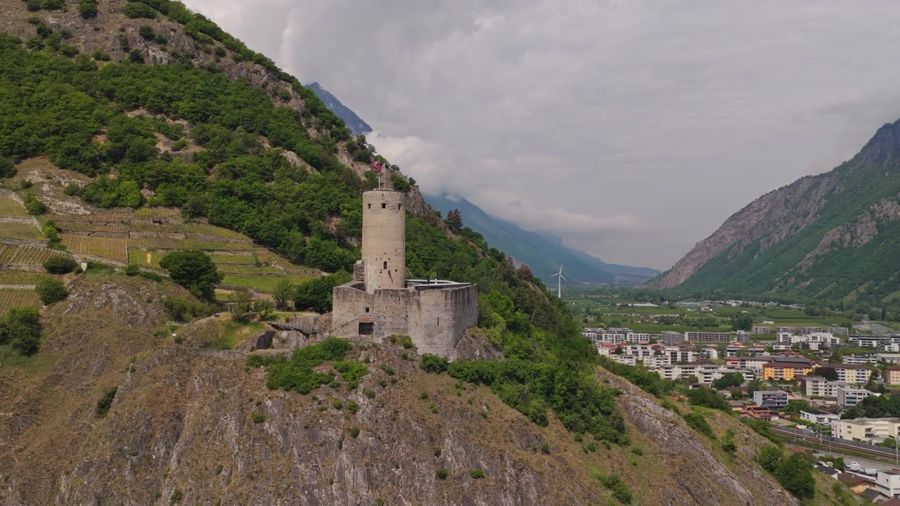 Filmato cinematografico con drone del Castello de la Bâtiaz a Martigny, Svizzera, che mostra la storica torre medievale, le montagne circostanti e le viste panoramiche sulla città alpina in una giornata di sole splendente.