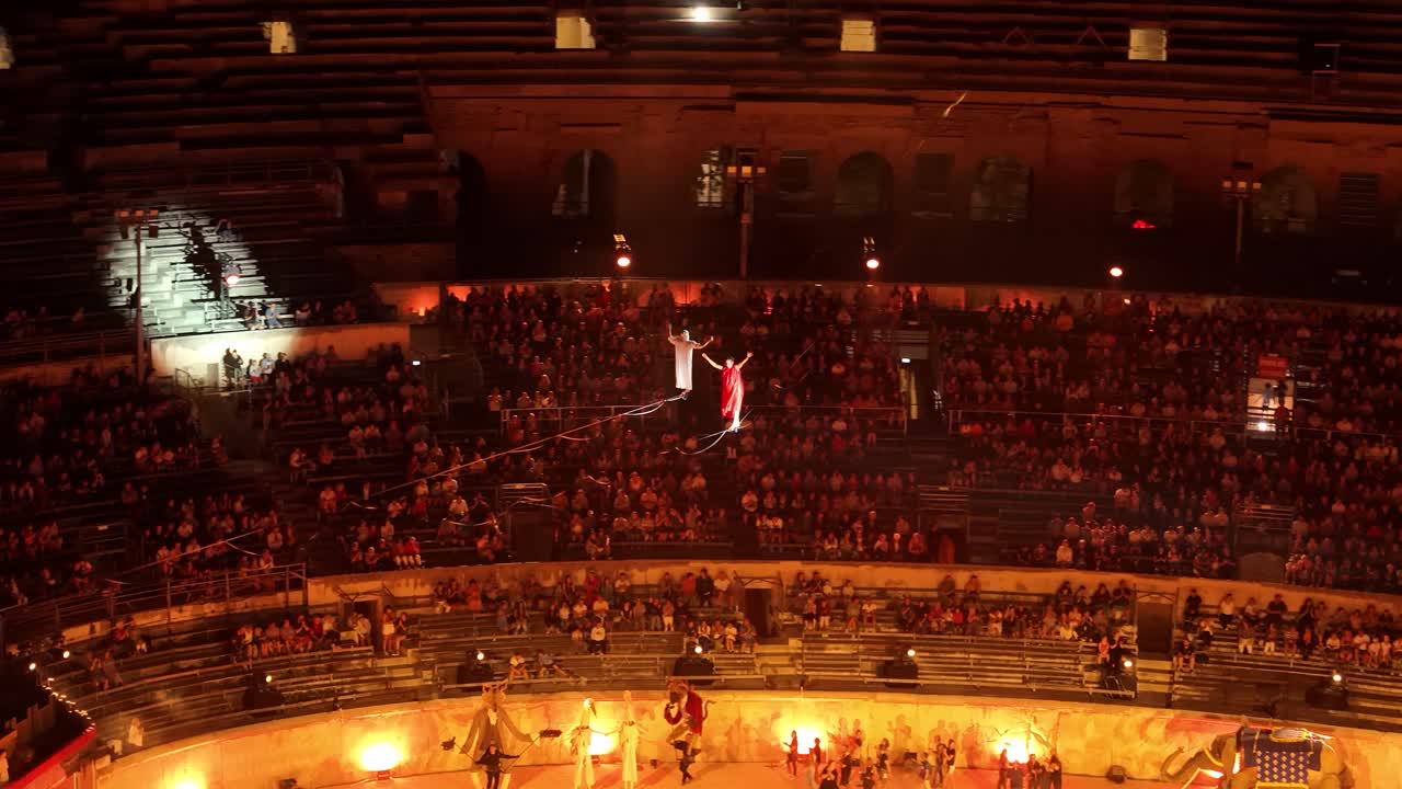 Aerial above people tightrope walking above the Nimes Arena as Performance to an audience.