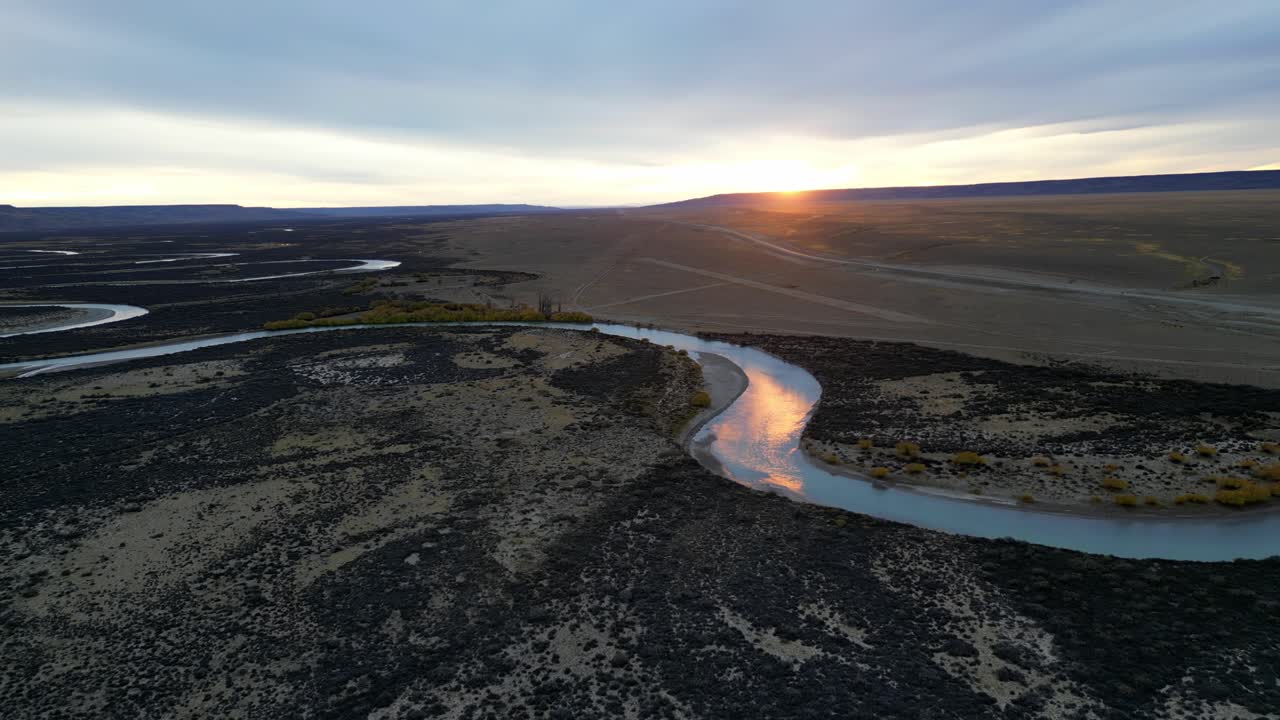 Cinematic landscape of Patagonia at sunset, with a shimmering blue river flowing across the endless Pampa