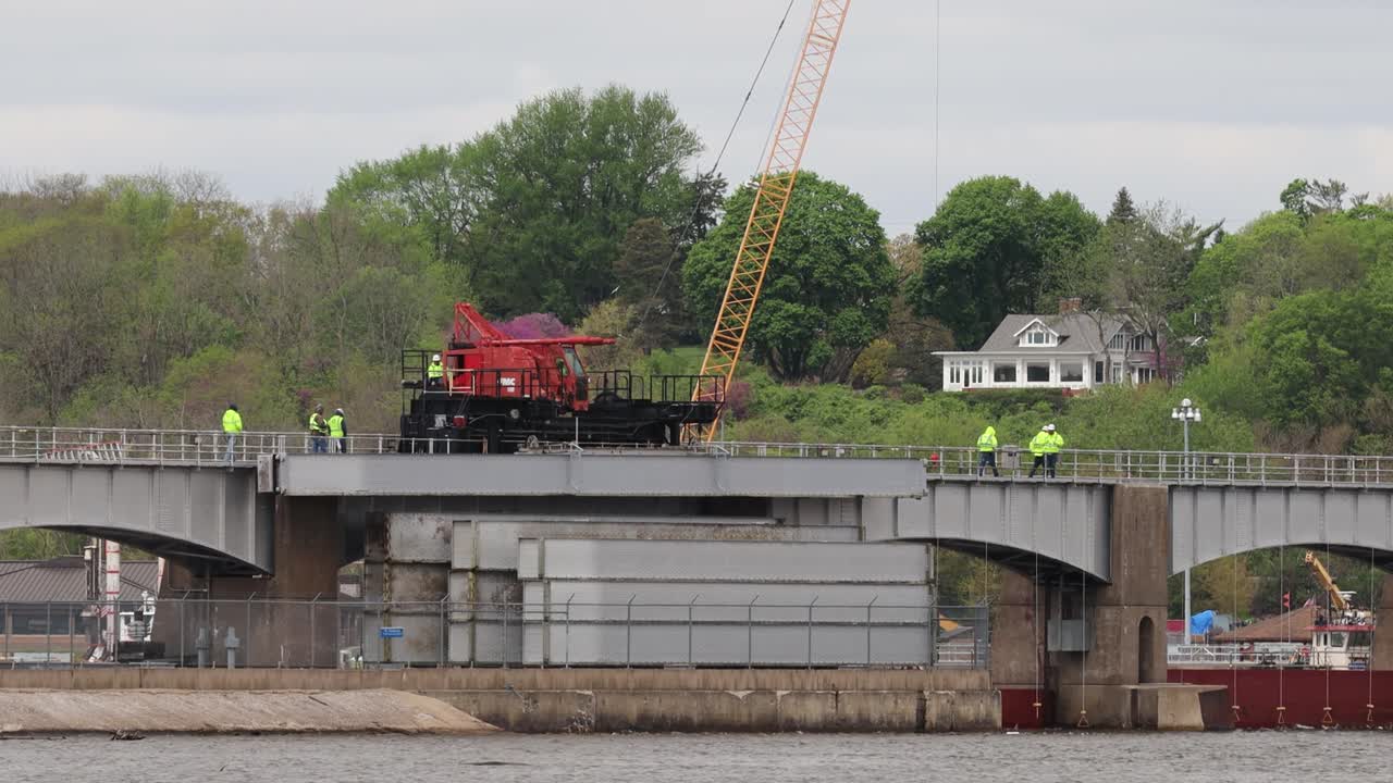 Small crew of men walking along side a moving crane to watch the dam rollers before lowering them into position at Lock and Dam Number 14 on the Mississippi River, near LeClair, Iowa USA