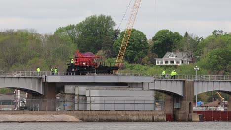 small crew of men walking along side a moving crane to watch the dam rollers before lowering them into position at lock and dam number 14 on the mississippi river, near leclair, iowa usa