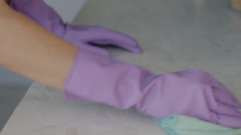 woman cleaning kitchen countertop with purple gloves