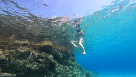 a young girl swims on the surface, underwater view from below, scuba diving on vacation