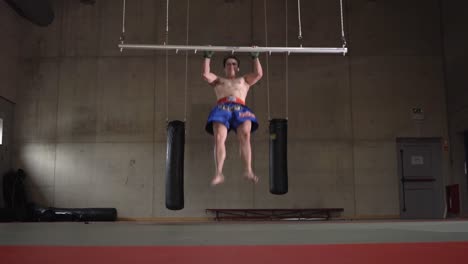 caucasian male doing burpees and pull ups in an empty boxing gym