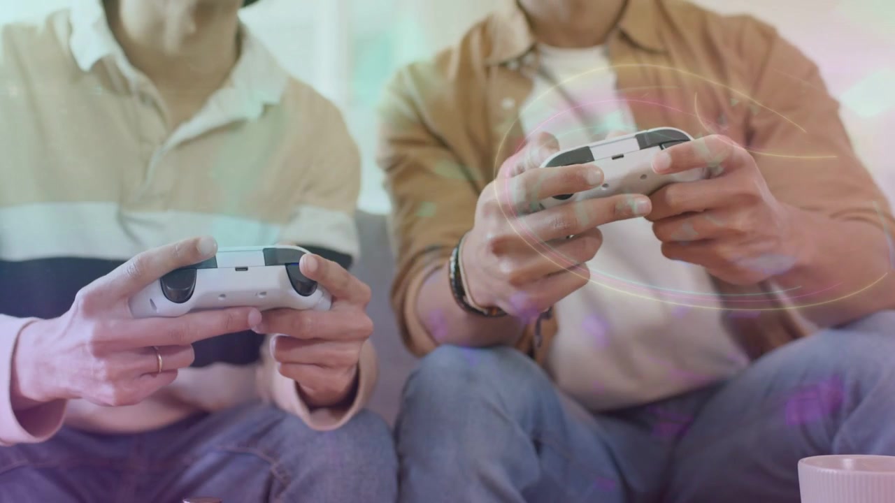 Dos hombres en un sofá sostienen controles, moviendo los pulgares y enviando comandos, con un efecto visual de destello sobre sus manos, mientras disfrutan de una sesión de juego.