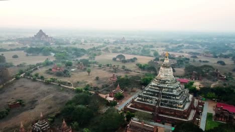 aerial view of the historic pagodas and temples scattered across the ancient plains of bagan, myanmar, with lush trees and golden morning light creating a serene and timeless landscape