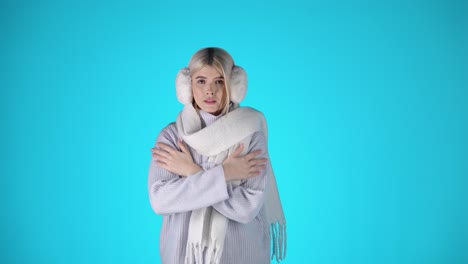 young pretty woman feeling cold, rubs hands on sleeves, studio shot with blue background