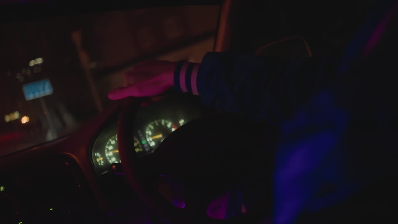 어둠 속에서 운전하는 백인 남성, 핸들을 잡은 손과 흐릿한 도시의 불빛, 클로즈업된 대시보드 보케와 은은한 광채, 익명의 밤의 라이더, 주의 깊은 조종사, 고독한 방랑자의 친밀한 내부로 묘사