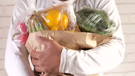 person holding a paper bag with wrapped vegetables