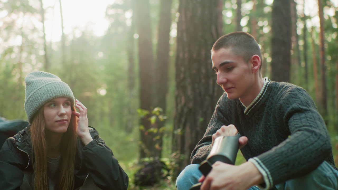 Lady gazes at boyfriend in flirty manner as he focuses on pumping air during outdoor activity, capturing playful moment and emotional connection with nature in background