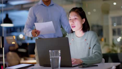 Focused-diverse-male-and-female-colleague-discussing-work-and-using-laptop-at-night-in-office