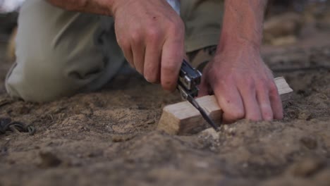 hombre caucásico sobreviviente cortando la muesca en el tablero de fuego en el campamento en el desierto