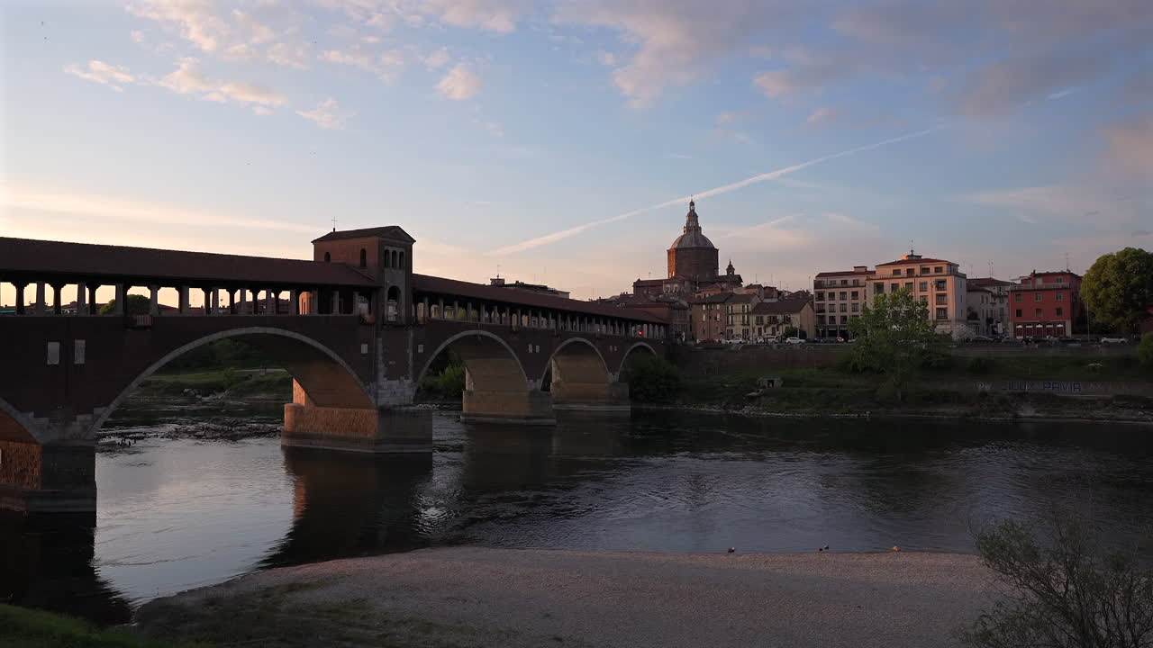 Skyline of Pavia , Ponte Coperto(covered bridge) is a bridge over the Ticino river in Pavia at sunset, Pavia Cathedral background, Italy at 30 fps