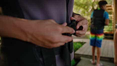 Male-hands-clasping-buckle-on-life-jacket-flotation-device-while-standing-on-dock-near-the-water-in-slow-motion