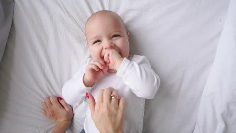 Baby-in-white-t-shirt-lying-on-a-white-bed-and-laughing-looking-at-the-camera-top-view-slow-motion