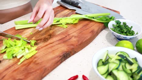 hands skillfully chop celery on a wooden board, surrounded by fresh ingredients in a well-lit kitchen