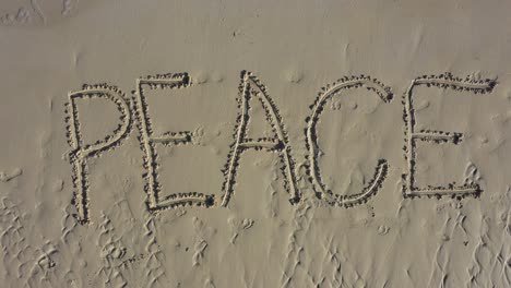 static shot of peace inscribed in the sand on a beach