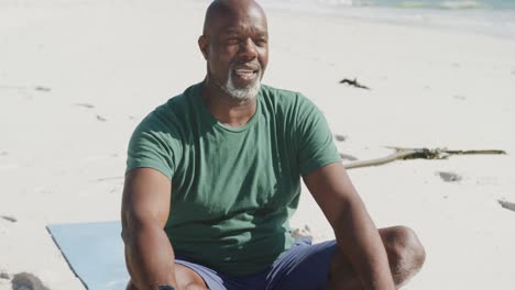 happy senior african american man doing yoga at beach, in slow motion