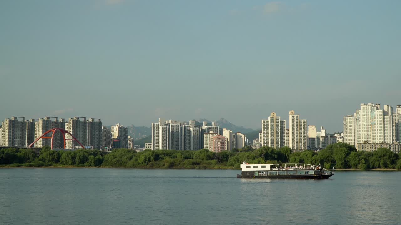 Ferry Cruise Ship Sailing on Hangang River along Bamseom Island with Seoul Urban High-Raised Apartment Buildings, Seogang Bridge and Bukhansan Mountains on Background, Tourism in South Korea daytime