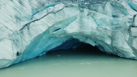 giant ice cave in a glacier melting in a lake below due to climate change in the alps, view from above