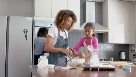happy biracial mother and daughter making cake mix, baking in kitchen, slow motion