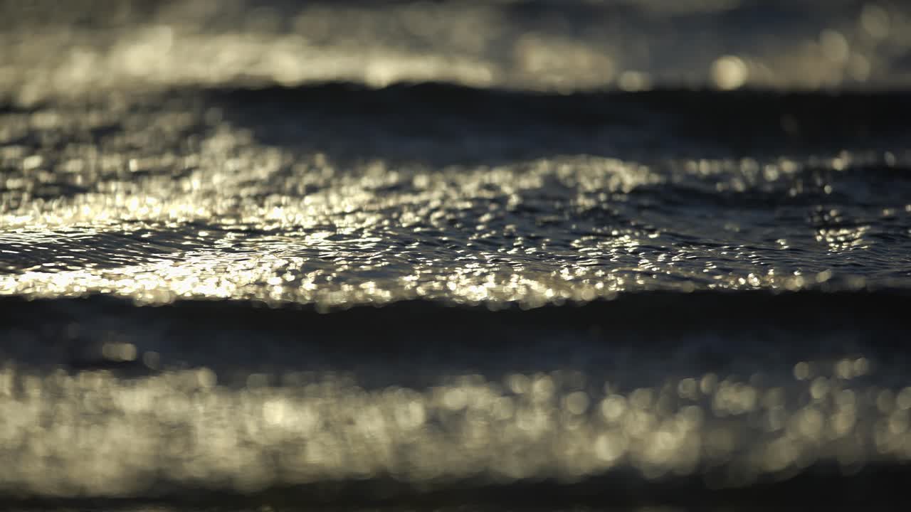 olas brillantes al atardecer rodando en una playa ventosa, vista abstracta de teleobjetivo