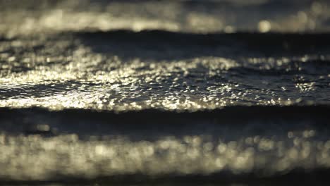 Shimmering-waves-at-sunset-rolling-in-onto-windy-beach,-abstract-telephoto-view