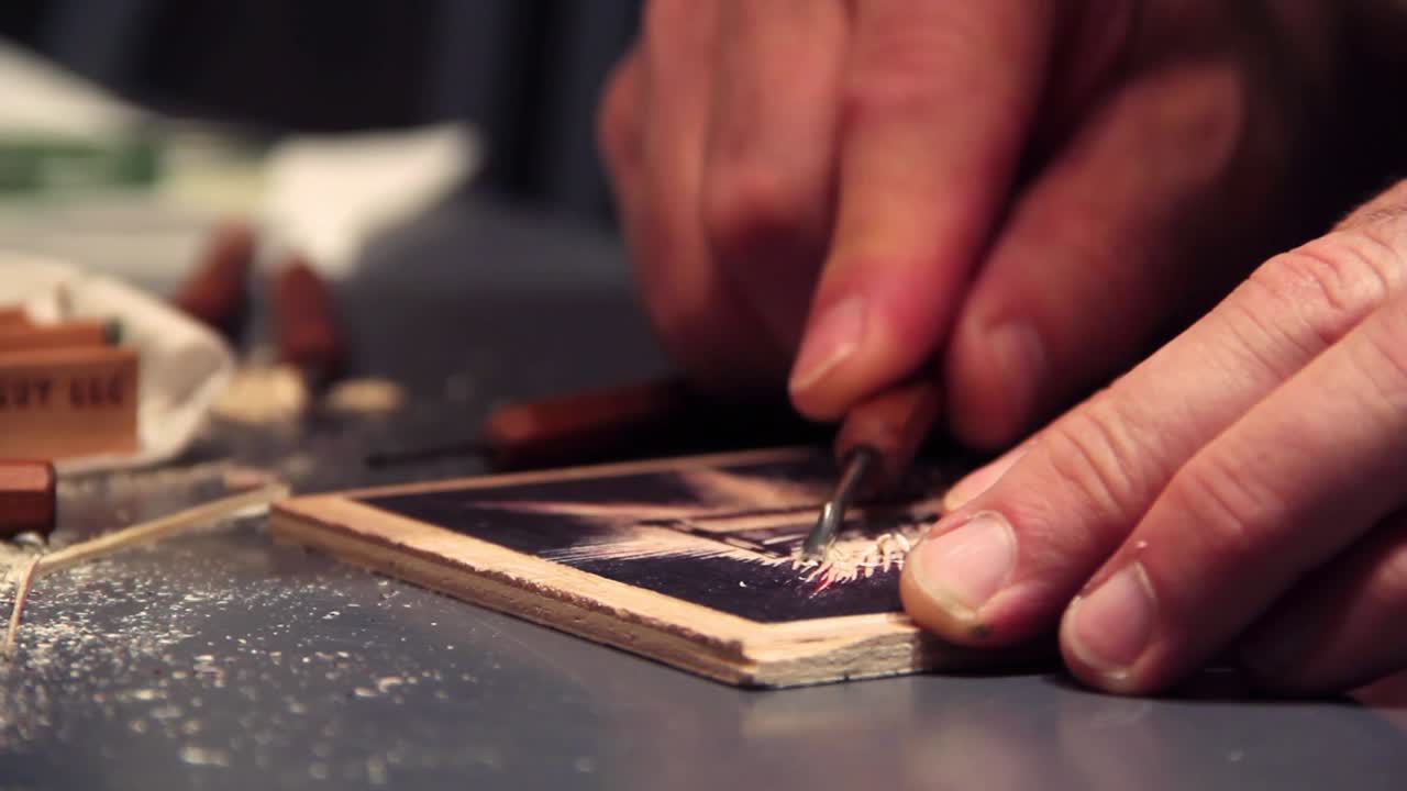 Artist carves a woodblock print with carving tools in the background.